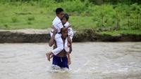 Seorang warga menggendong siswa Sekolah Dasar Negeri (SDN) 6 Tapa saat melintasi sungai Polanggua di Dusun III, Desa Langge, Tapa, Kabupaten Bone Bolango, Gorontalo, Rabu (29/7/2020).