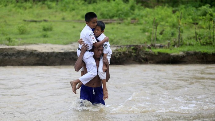 SISWA DAN GURU MENYEBERANGI SUNGAI UNTUK BELAJAR MENGAJAR Seorang warga menggendong siswa Sekolah Dasar Negeri (SDN) 6 Tapa melintasi sungai Polanggua bersama sejumlah guru usai mengikuti pelajaran luar jaringan (luring) di Dusun III, Desa Langge, Tapa, Kabupaten Bone Bolango, Gorontalo, Rabu (29/7/2020). Guru dan siswa harus melintasi sungai untuk melakukan aktivitas belajar mengajar karena belum tersedianya jembatan menuju dusun III tersebut . ANTARA FOTO/Adiwinata Solihin/aww.