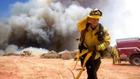 Seorang petugas pemadam kebakaran membawa selang air saat tengah berupaya memadamkan api yang menjalar di kawasan California, Amerika Serikat, pada Sabtu (1/8/2020) waktu setempat.