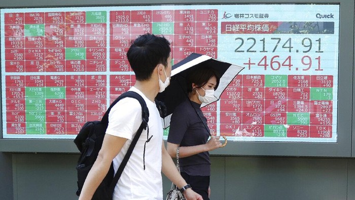 People wearing face masks walk by an electronic stock board of a securities firm in Tokyo, Monday, Aug. 3, 2020. Asian shares were mixed on Monday, as investors watched surging numbers of new coronavirus cases in the region, including in Japan. (AP Photo/Koji Sasahara)