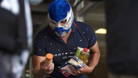 Seorang pegulat dari Lucha Libre, Meksiko, memeriksa isi paket makanannya.  