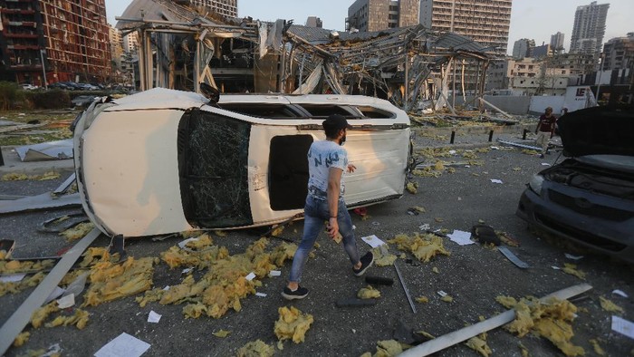 BEIRUT, LEBANON - AUGUST 04: A man walks by an overturned car and destroyed buildings on August 4, 2020 in Beirut, Lebanon. At least 50 people were killed and thousands more injured when two explosions occurred near the Lebanese capitals port area.  (Photo by Marwan Tahtah/Getty Images)