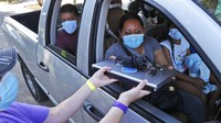 Wearing a mask to prevent the spread of COVID-19, Megan Steckly, CEO of Com-U-Dot, checks a driver in a line of cars as they wait to receive a computer during a drive through event in Dallas, Tuesday, Aug. 4, 2020. TXU Energy and Comp-U-Dopt partnered with the City of Dallas to give away 400 computers to middle school students to use when school starts. (AP Photo/LM Otero)