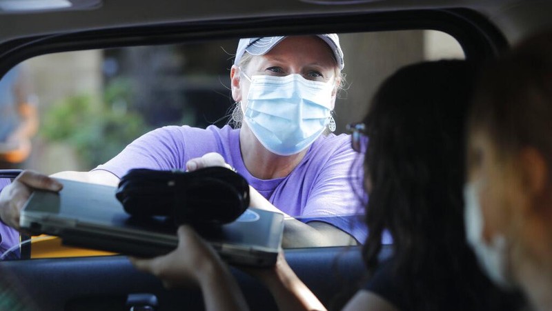 Wearing a mask to prevent the spread of COVID-19, Megan Steckly, CEO of Com-U-Dot, checks a driver in a line of cars as they wait to receive a computer during a drive through event in Dallas, Tuesday, Aug. 4, 2020. TXU Energy and Comp-U-Dopt partnered with the City of Dallas to give away 400 computers to middle school students to use when school starts. (AP Photo/LM Otero)