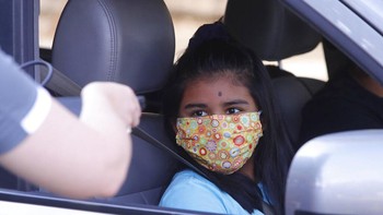 Dengan mengenakan masker untuk mencegah penyebaran COVID-19, seorang siswa menunggu untuk menerima komputer portabel selama acara di Dallas, Texas (AP Photo/LM Otero)