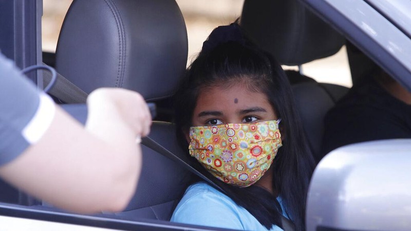 Wearing a mask to prevent the spread of COVID-19, Megan Steckly, CEO of Com-U-Dot, checks a driver in a line of cars as they wait to receive a computer during a drive through event in Dallas, Tuesday, Aug. 4, 2020. TXU Energy and Comp-U-Dopt partnered with the City of Dallas to give away 400 computers to middle school students to use when school starts. (AP Photo/LM Otero)