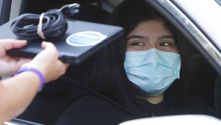 Wearing a mask to prevent the spread of COVID-19, Megan Steckly, CEO of Com-U-Dot, checks a driver in a line of cars as they wait to receive a computer during a drive through event in Dallas, Tuesday, Aug. 4, 2020. TXU Energy and Comp-U-Dopt partnered with the City of Dallas to give away 400 computers to middle school students to use when school starts. (AP Photo/LM Otero)