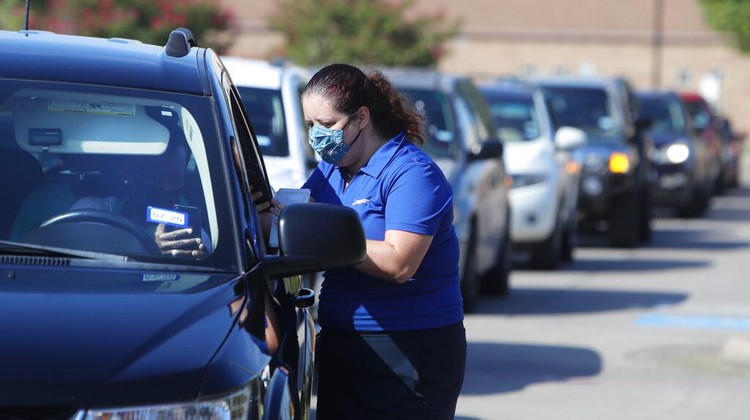 Wearing a mask to prevent the spread of COVID-19, Megan Steckly, CEO of Com-U-Dot, checks a driver in a line of cars as they wait to receive a computer during a drive through event in Dallas, Tuesday, Aug. 4, 2020. TXU Energy and Comp-U-Dopt partnered with the City of Dallas to give away 400 computers to middle school students to use when school starts. (AP Photo/LM Otero)