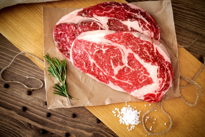 Two raw rib eye steak on a wooden Board on a table prepared for the grill. Top view rustic style