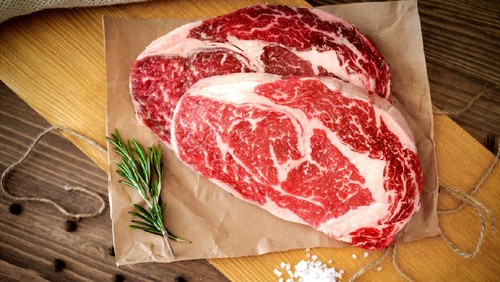 Two raw rib eye steak on a wooden Board on a table prepared for the grill. Top view rustic style