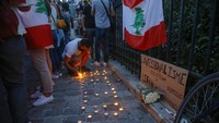 Seorang pria dari komunitas Lebanon menyalakan lilin di samping bendera Lebanon untuk mengenang para korban ledakan mematikan di Beirut di Paris, Prancis. AP Photo/Michel Euler  