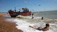 Anak-anak bermain di laut saat kapal nelayan kembali dari laut di Hastings, Inggris. Dan Kitwood/Getty Images  