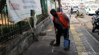 Seorang warga yang terjaring razia penindakan pelanggaran aturan Pembatasan Sosial Berskala Besar (PSBB) oleh Satpol PP menjalani hukuman dengan membersihkan trotoar di Kampung Melayu, Jakarta, Jumat (7/8/2020).