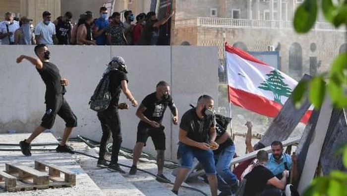 Lebanese protesters duck for cover during clashes with security forces in downtown Beirut on August 8, 2020, following a demonstration against a political leadership they blame for a monster explosion that killed more than 150 people and disfigured the capital Beirut. (Photo by - / AFP)