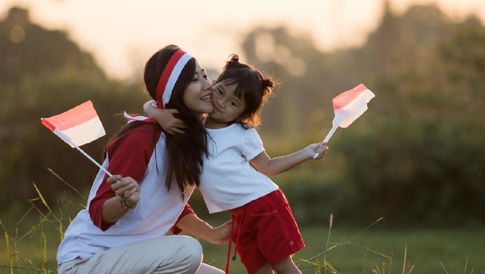 Beautiful young mother with her daughter celebrating indonesia independence day by raising flag under the sunset sky