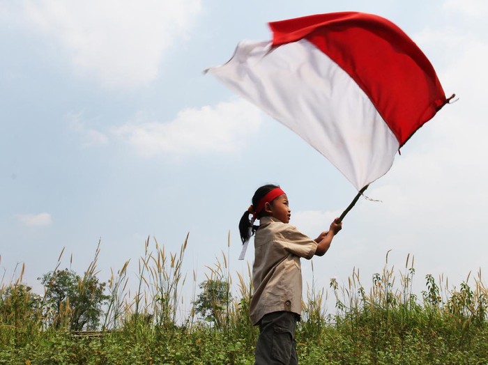 Beautiful young mother with her daughter celebrating indonesia independence day by raising flag under the sunset sky