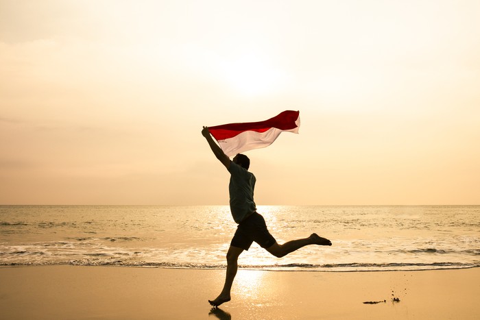 Bendera merah putih young man running on the beach carrying Indonesia flag