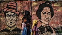 Warga melintasi mural bergambar Pattimura dan Cut Nyak Dien.  