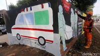 Mural itu bergambar tim medis ber-APD lengkap sedang memakamkan jenazah COVID-19. Sementara di sisi lain bergambar mobil jenazah.