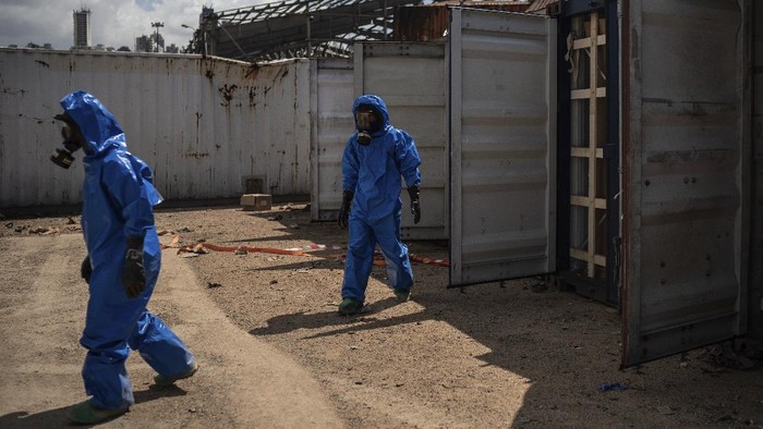 French emergency workers, part of a special unit working with chemicals, walk next to damaged containers near the site of last weeks explosion, in the port of Beirut, Lebanon, Monday, Aug. 10, 2020. The unit is identifying potential leaks and securing an area where containers with flammable liquids have been damaged by the blast. (AP Photo/Felipe Dana)