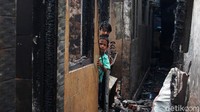 Dua orang anak beraktivitas di rumahnya yang telah hangus terbakar.