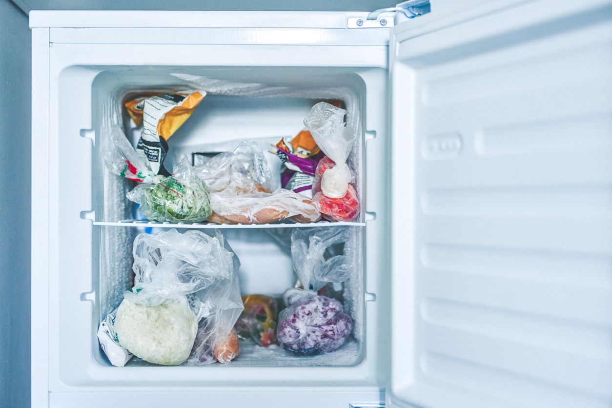 Shot of an open freezer packed with frozen food in plastic bags