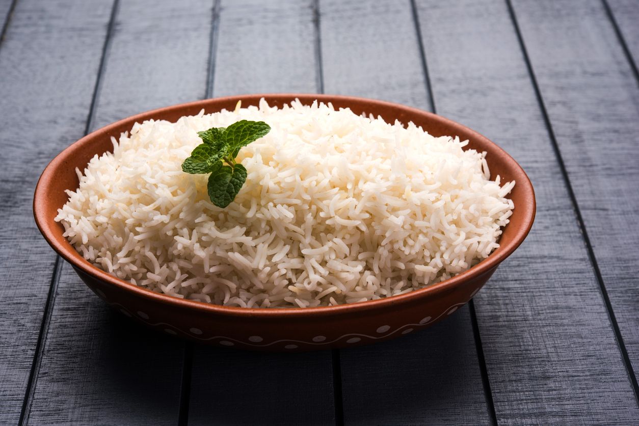 A bowl of steamed white rice in a Padang eatery. The cooked rice is served in a big bowl that serves several portion for a group of diners. In the background is Padang side dishes that accompanies the rice.