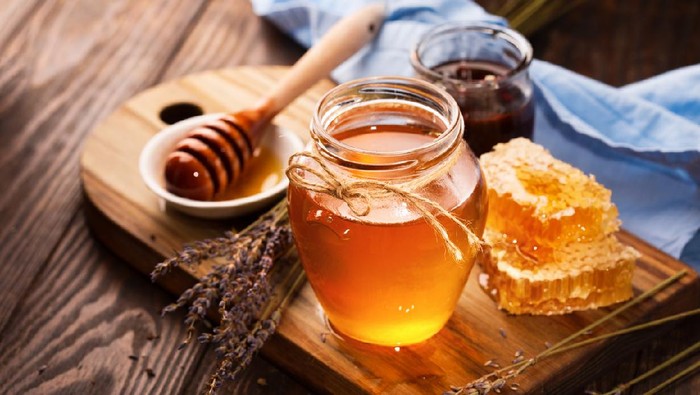 Jar of liquid honey with honeycomb inside and bunch of dry lavender over old wooden table. Dark rustic style, selective focus