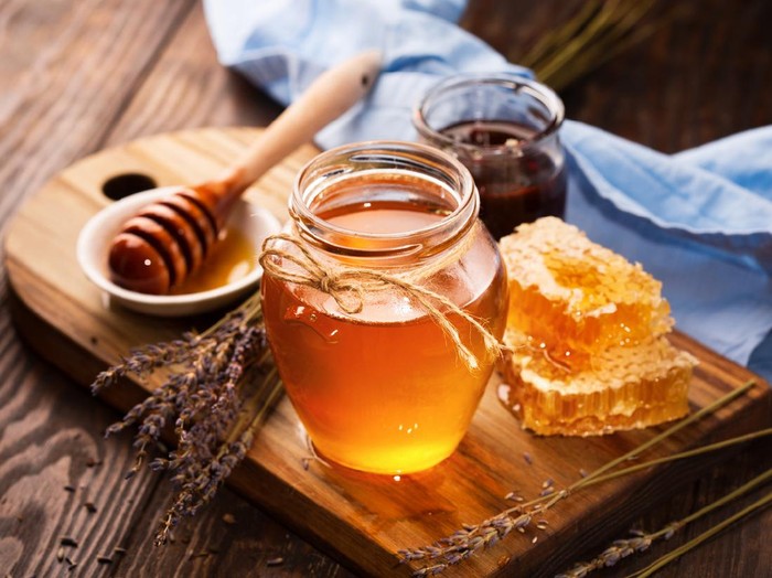 Jar of liquid honey with honeycomb inside and bunch of dry lavender over old wooden table. Dark rustic style, selective focus