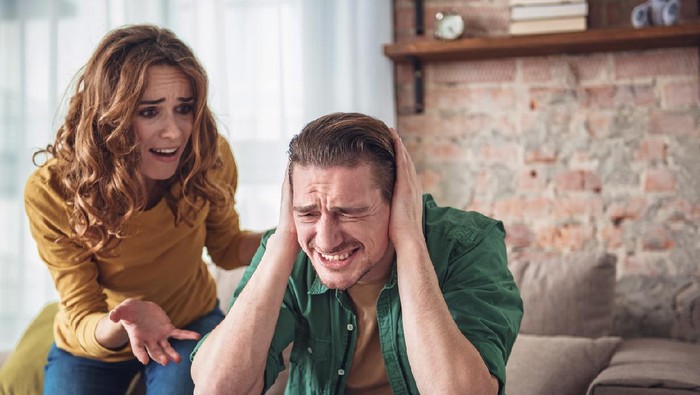 Listen to me. Angry man is closing his ears with desperation while his wife is shouting at him. Family conflict concept