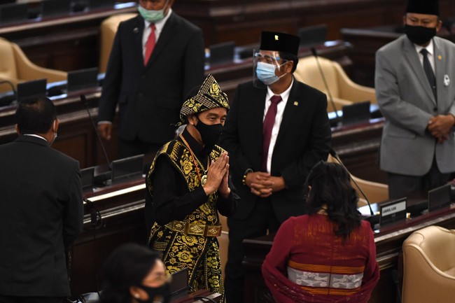 Orang nomor satu di Indonesia ini lalu menyempurnakan gayanya dengan sebuah sabuk emas dan kalung senada. Tidak ketinggalan sebuah ikat kepala yang meruncing ke atas. Mengedepankan protokol kesehatan, Jokowi tetap memakai masker berwarna hitam sehingga tetap senada dengan busananya. (Foto: ANTARA FOTO/AKBAR NUGROHO GUMAY)