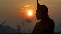 Seorang warga Suku Amazon tampak mengenakan hiasan kepala tradisional dari bulu dan cat tubuh saat melakukan aksi blokir jalan di kawasan Brasil.