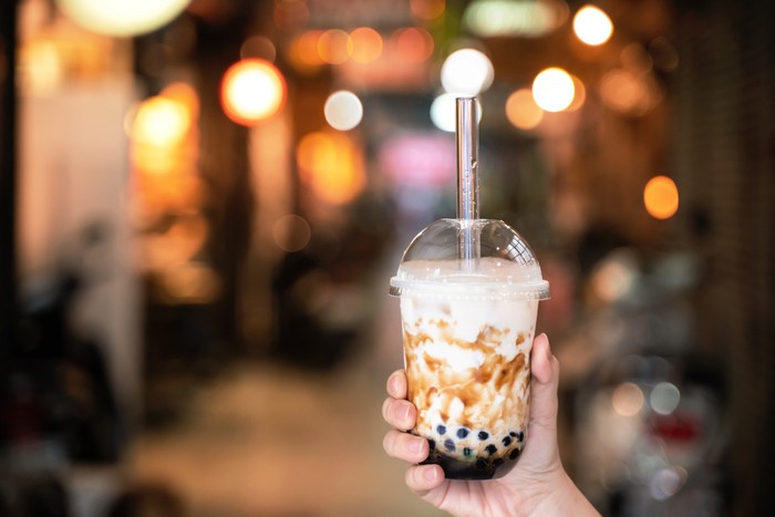 Boba Young girl in denim jacket is drinking brown sugar flavored tapioca pearl bubble milk tea with glass straw in night market of Taiwan, close up, bokeh