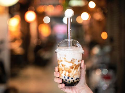 Young girl in denim jacket is drinking brown sugar flavored tapioca pearl bubble milk tea with glass straw in night market of Taiwan, close up, bokeh