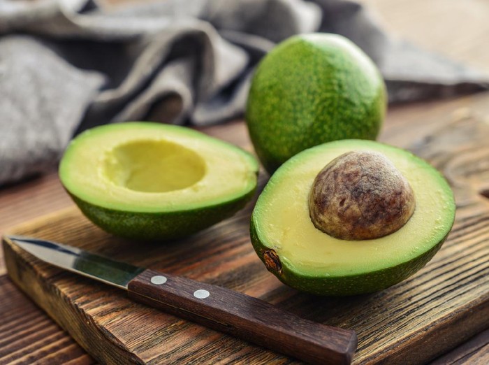 Avocado on old wooden table in bowl. Halfs of avocados fresh fruits healthy food.