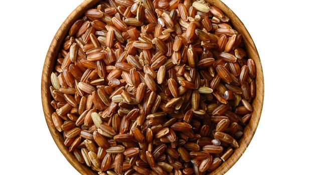 Wooden bowl with uncooked brown rice isolated on white background. Top view
