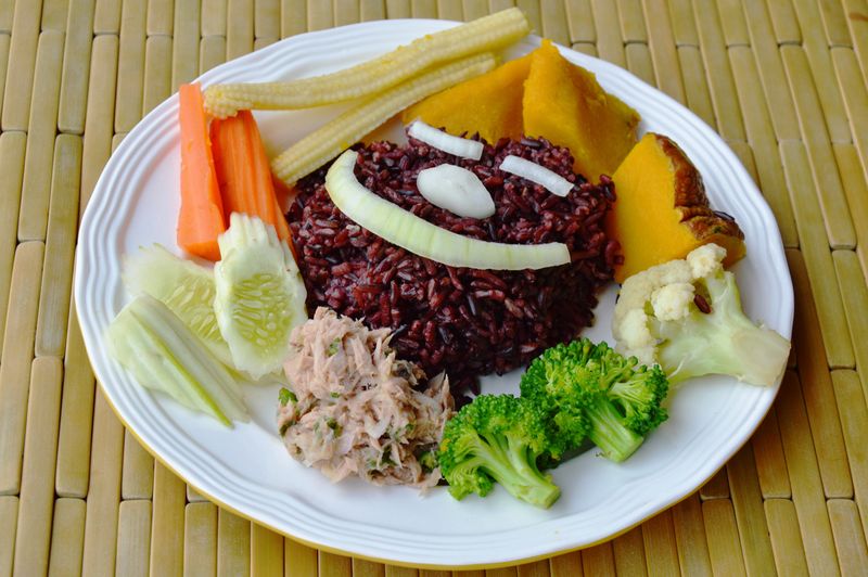 Wooden bowl with uncooked brown rice isolated on white background. Top view