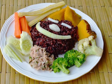 Wooden bowl with uncooked brown rice isolated on white background. Top view