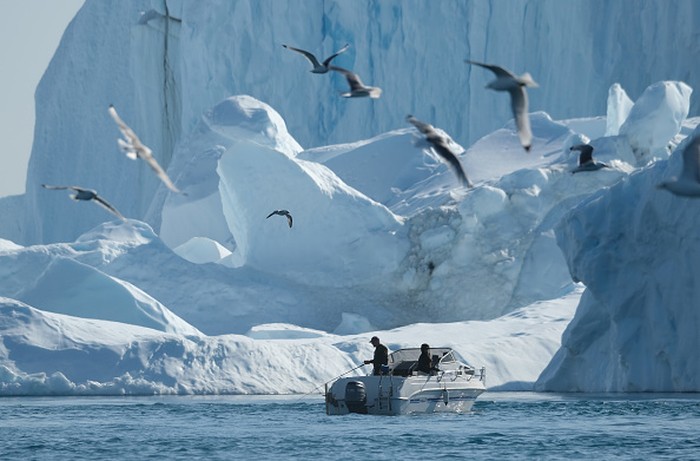 ILULISSAT, GREENLAND - JULY 30: An iceberg floats in Disko Bay behind houses during unseasonably warm weather on July 30, 2019 in Ilulissat, Greenland. The Sahara heat wave that recently sent temperatures to record levels in parts of Europe is arriving in Greenland. Climate change is having a profound effect in Greenland, where over the last several decades summers have become longer and the rate that glaciers and the Greenland ice cap are retreating has accelerated.   (Photo by Sean Gallup/Getty Images)