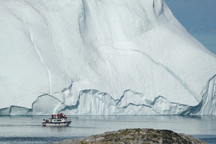 ILULISSAT, GREENLAND - JULY 30: An iceberg floats in Disko Bay behind houses during unseasonably warm weather on July 30, 2019 in Ilulissat, Greenland. The Sahara heat wave that recently sent temperatures to record levels in parts of Europe is arriving in Greenland. Climate change is having a profound effect in Greenland, where over the last several decades summers have become longer and the rate that glaciers and the Greenland ice cap are retreating has accelerated.   (Photo by Sean Gallup/Getty Images)