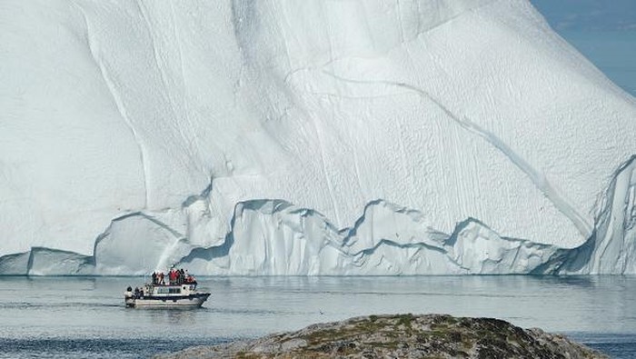ILULISSAT, GREENLAND - JULY 30: An iceberg floats in Disko Bay behind houses during unseasonably warm weather on July 30, 2019 in Ilulissat, Greenland. The Sahara heat wave that recently sent temperatures to record levels in parts of Europe is arriving in Greenland. Climate change is having a profound effect in Greenland, where over the last several decades summers have become longer and the rate that glaciers and the Greenland ice cap are retreating has accelerated.   (Photo by Sean Gallup/Getty Images)