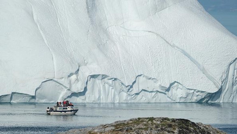 Lapisan Es Greenland Mencair ILULISSAT, GREENLAND - JULY 30: An iceberg floats in Disko Bay behind houses during unseasonably warm weather on July 30, 2019 in Ilulissat, Greenland. The Sahara heat wave that recently sent temperatures to record levels in parts of Europe is arriving in Greenland. Climate change is having a profound effect in Greenland, where over the last several decades summers have become longer and the rate that glaciers and the Greenland ice cap are retreating has accelerated. (Photo by Sean Gallup/Getty Images)