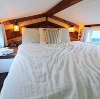 Siapa sangka jika rumah mungil ini memiliki lantai dua. Pada lantai dua, ada tempat tidur nyaman yang menjadi tempat Jonathan dan Yunae beristirahat. Jendela di sisi kiri dan kanan menjadi pelengkap ruangan yang membuat mereka betah berada di kamar. Dengan jendela tersebut sinar matahari bisa masuk dengan mudah dan jika hujan tiba mereka bisa tetap menikmati keindahan alam di luar sambil berbaring di tempat tidur. Foto: Youtube Living Big In A Tiny House