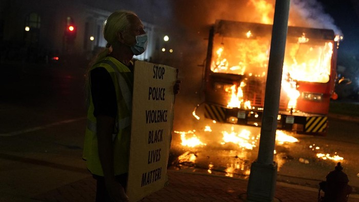 A protester stands near a burning garbage truck outside the Kenosha County Courthouse, late Monday, Aug. 24, 2020, in Kenosha, Wis. Protesters converged on the county courthouse during a second night of clashes after the police shooting of Jacob Blake a day earlier turned Kenosha into the nation’s latest flashpoint city in a summer of racial unrest. (AP Photo/David Goldman)