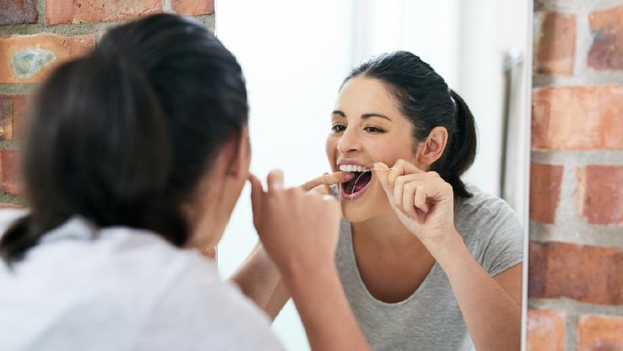 Dental flossing Shot of a beautiful young woman flossing her teeth in the bathroom mirror