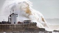 Warga melihat gelombang ombak besar saat menghantam mercusuar dan tanggul laut di Porthcawl di Wales selatan, Inggris. Getty Images/Dan Kitwood  