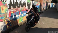 Seorang pengendara motor melintas di depan mural. Mural menggambarkan keakraban masyarakat dalam berbagai perbedaan keyakinan dan agamanya di bawah naungan Pancasila.