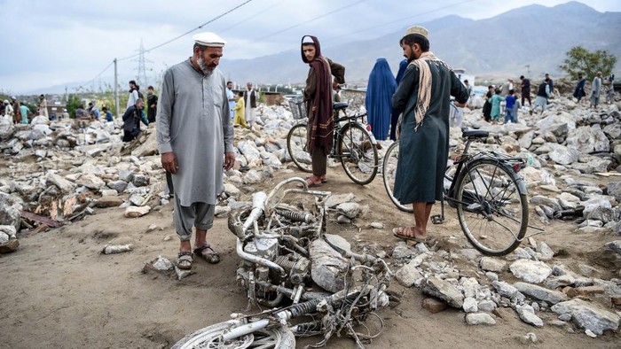 A villager (L) stands next to a destroyed motorbike as residents gather among the debris of their houses after a flash flood affected the area at Sayrah-e-Hopiyan in Charikar, Parwan province, on August 26, 2020. - The death toll from flash floods that swept through an Afghan city climbed to 100 on August 26, officials said, as rescue workers searched for survivors in the rubble of collapsed houses. (Photo by WAKIL KOHSAR / AFP)