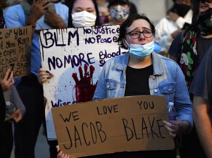 A protester holds up a phone as he stands in front of authorities Tuesday, Aug. 25, 2020, in Kenosha, Wis. Anger over the Sunday shooting of Jacob Blake, a Black man, by police spilled into the streets for a third night. (AP Photo/Morry Gash)