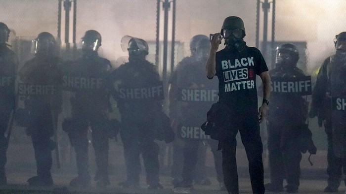A protester holds up a phone as he stands in front of authorities Tuesday, Aug. 25, 2020, in Kenosha, Wis. Anger over the Sunday shooting of Jacob Blake, a Black man, by police spilled into the streets for a third night. (AP Photo/Morry Gash)